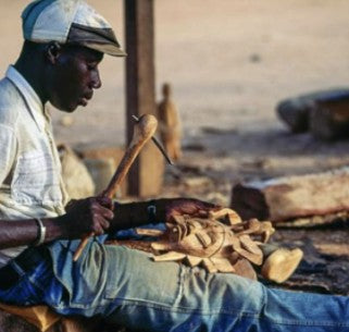 A carver shaping a wooden mask with a mallet and chisel