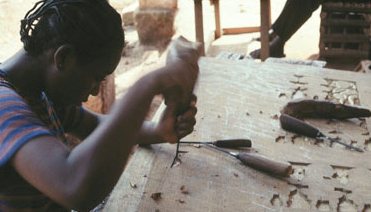 A carver cutting a pattern into a wooden panel with a chisel