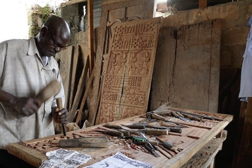 A carver working with a mallet and chisel, a carved wooden door behind him