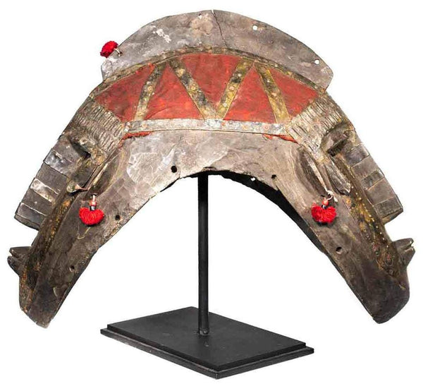 Dogon Mask, made from wood, metal and cloth in Mali, with a face on each end and red tassels, shown on its custom stand