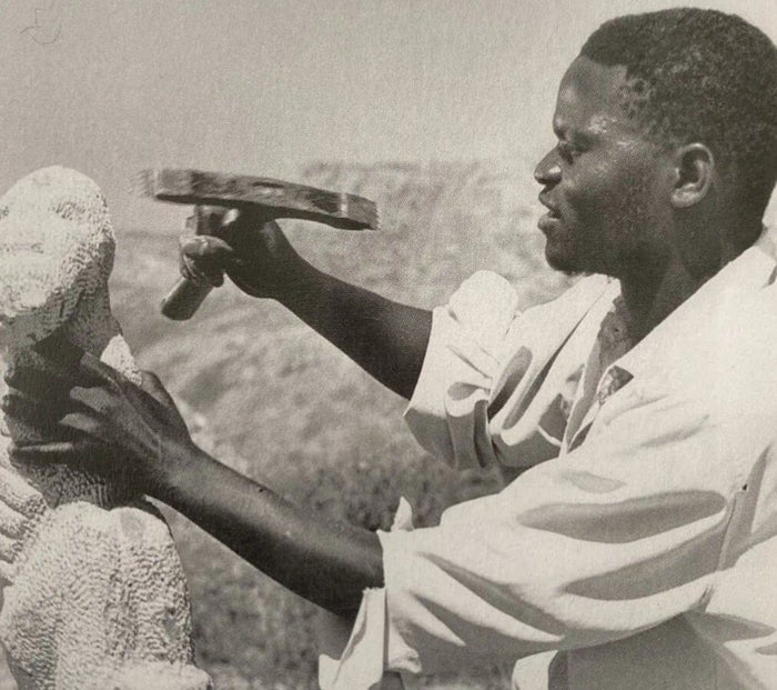 A Shona sculptor shaping a block of stone with a hammer