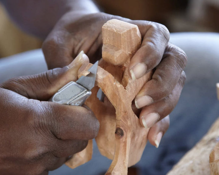 Hands carving a small wooden figure with a knife