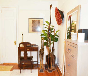 Giraffe carvings in a bedroom corner beside a writing desk, a mirror and a red feather wall hanging