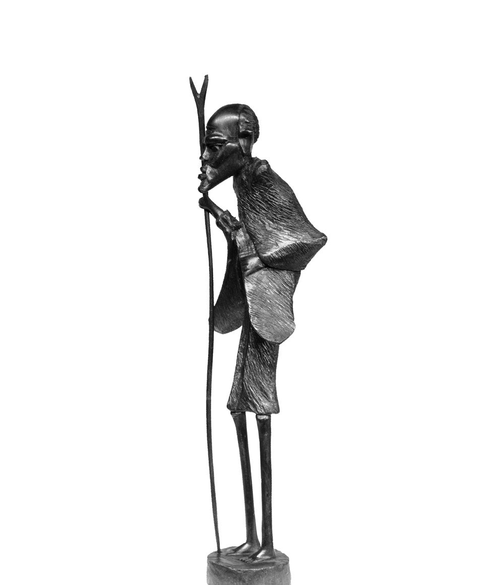 Masaai Old Man, an elder in a draped cloak leaning on his staff, carved from ebony wood in Kenya by the artist Nelson